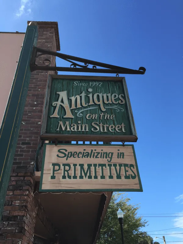 A hand-painted hanging sign for an antiques shop on a brick building downtown.