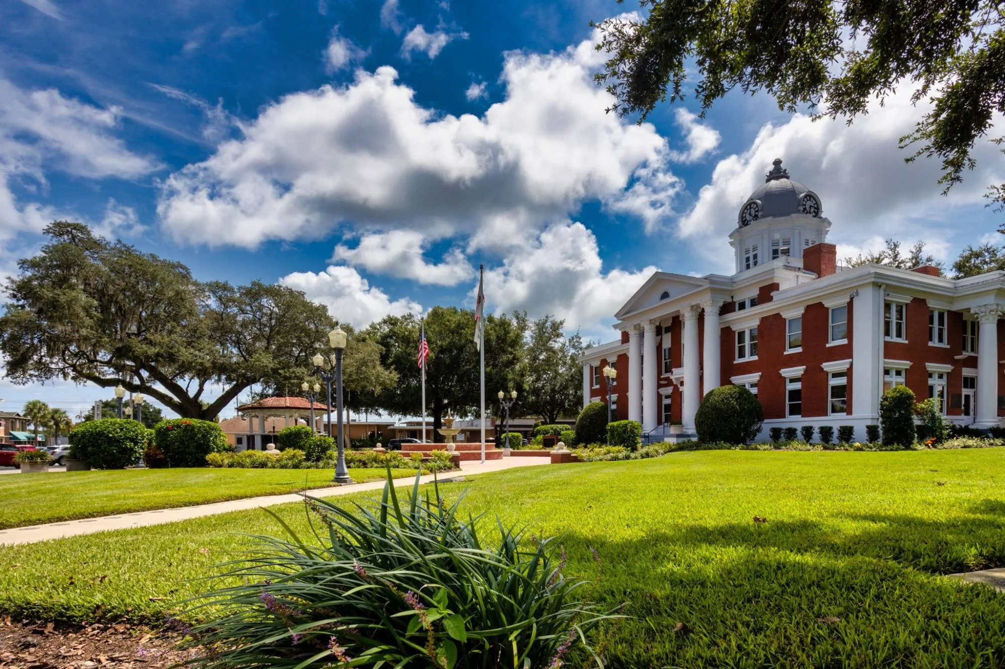 The 1909 Pasco County Courthouse under a summer sky, with the lawn, live oaks and bandstand of the courthouse square.