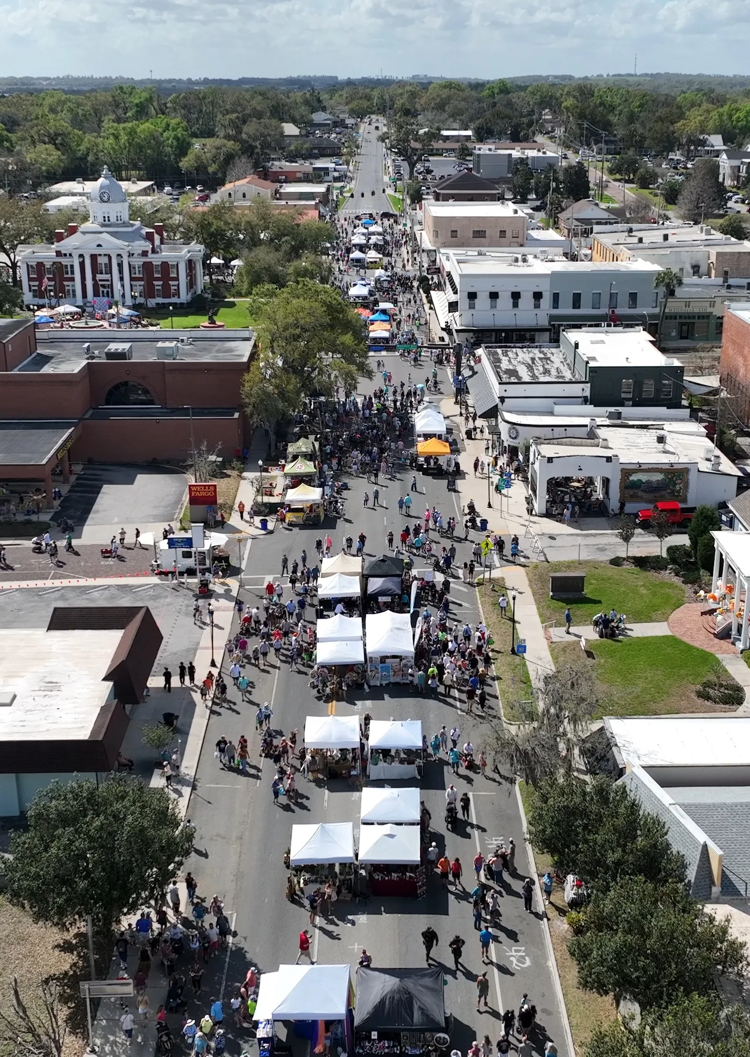 Aerial view of the 2026 Kumquat Festival: white vendor tents and crowds filling 7th Street, with the 1909 courthouse on the left.